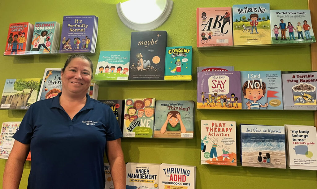 Sarah Bright, Education Coordinator at the Bay Area Hospital’s Kids’ HOPE Center in Coos Bay, stands in front of their community lending library.